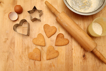 Top view of cutting cookies from metal molds in the form of heart on a wooden table.