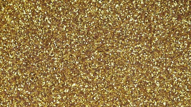 Top view of a surface made of fine sparkling gold glitter. Close-up background of shimmering golden glitter.
