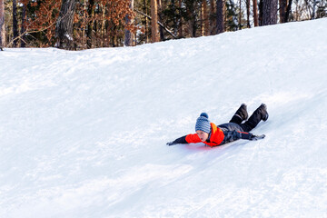 Boy sledding down the hills without sledge on a winter day.