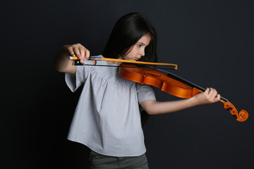 Preteen girl playing violin on black background