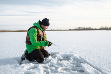 young man on a winter fishing trip on a snowy lake fishes on a fishing rod - Powered by Adobe