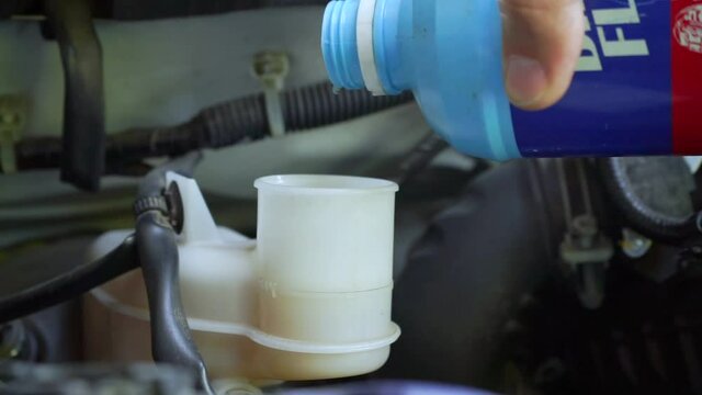 The auto mechanic is refilling additional brake fluid after the inspection and repair of the damaged parts.