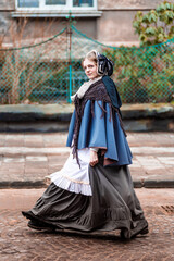 Nineteenth-century woman, elegantly dressed, walks through the courtyard of a castle.