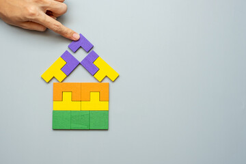hand connecting Home shape block with colorful wood puzzle pieces on gray background. logical...