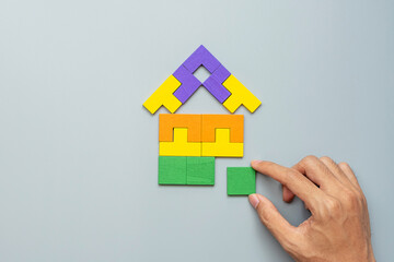 Fototapeta na wymiar hand connecting Home shape block with colorful wood puzzle pieces on gray background. logical thinking, business logic, solutions, rational, house, real estate and strategy concepts