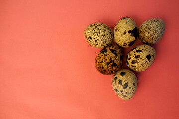 six raw quail eggs lie side by side in a triangle on a pink background top view