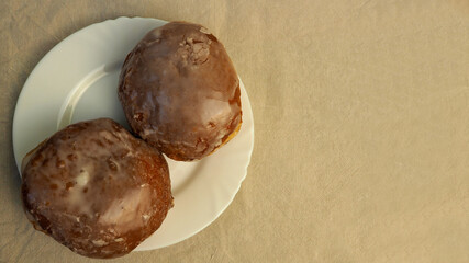 two sugar coated doughnuts lie in a white round plate view on a beige linen tablecloth view from above