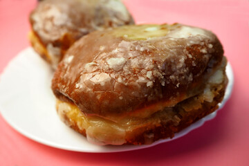 close up two donuts in sugar glaze lie in a white round plate on a pink background side view