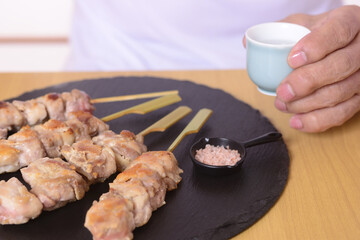 日本酒を呑むシニアの手と焼き鳥