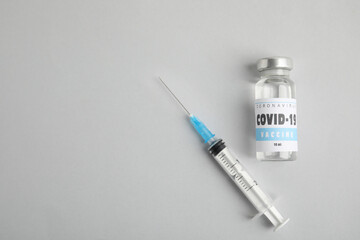 Vial with coronavirus vaccine and syringe on light background, flat lay. Space for text