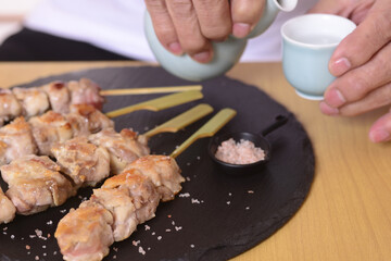 日本酒を呑むシニアの手と焼き鳥