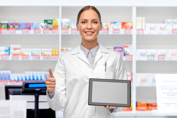 medicine, profession and healthcare concept - happy smiling female doctor or scientist in white coat with tablet pc computer showing thumbs up over pharmacy background