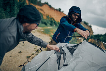 Two hikers adjusting tent on camping trip while standing in a nature.