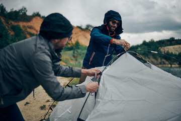 Two hikers adjusting tent on camping trip while standing in a nature.