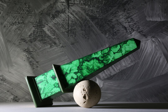 Obelisco in finta malachite in equilibrio precario su una sfera in pietra; oggetti in un interno su un fondo grigio scuro
