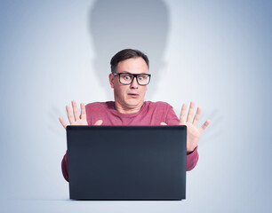 Scared man with glasses in front of laptop. Fear emotion concept