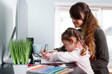 mother and little girl coloring with crayons while sitting together at their living table. early development concept.
