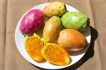 Colorful whole and halved delicious prickly pear fruits served on a white plate