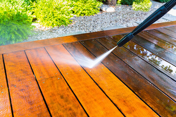 cleaning the terrace with a pressure washer - high-pressure cleaner on the wooden surface of the...