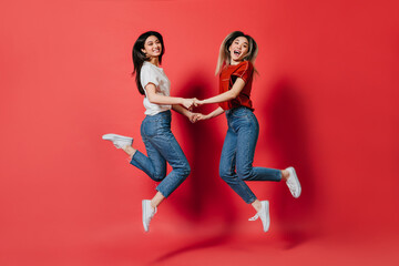 Fototapeta na wymiar Happy Asian women in stylish T-shirts and jeans trousers jumping on isolated background