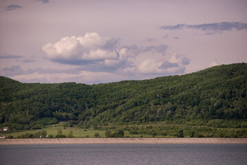 spring landscape with a high hill full of green forest on the edge of a huge lake. a sunny day on the bank of the reservoir