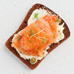 Smorrebrod - traditional Danish sandwiches. Black rye bread with salmon, cream cheese, capers on white background. Top view, close up