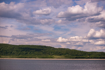 spring landscape with a high hill full of green forest on the edge of a huge lake. a sunny day on the bank of the reservoir