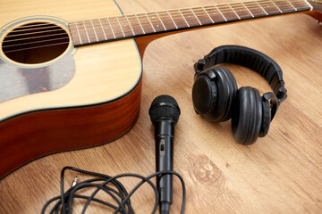 leisure, music and musical instruments concept - close up of acoustic guitar, microphone and headphones on black table