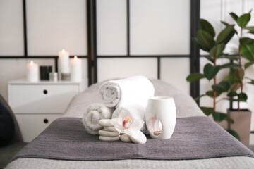 Fototapeta na wymiar Towels, aroma lamp, orchid flower and stones on couch in spa salon