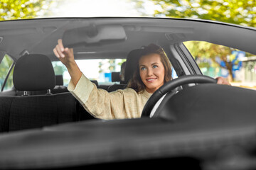 transportation, vehicle and people concept - happy smiling female driver adjusting mirror and driving car with male passenger