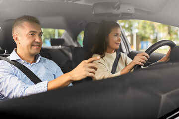 driver courses and people concept - car driving school instructor teaching young woman to drive