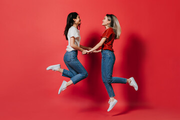 Fototapeta na wymiar Girls in jeans have fun and jump on red background