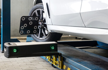 Car on wheel alignment station with sensor and laser reflector on wheel hub to check in workshop.
