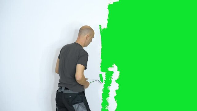 Fast time lapse 4k of mature adult man painting white wall in room with green color to create a greenscreen background, medium shot
