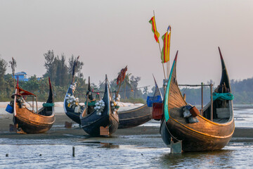 Landscape view of traditional wooden fishing boats known as moon boats glowing at sunset on beach near Cox's Bazar in southern Bangladesh