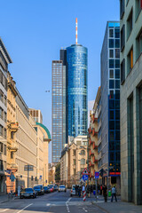 Street with cars in the city of Frankfurt. Commercial buildings along the street with a view of a skyscraper. High-rise building with glass facade in sunshine and blue sky