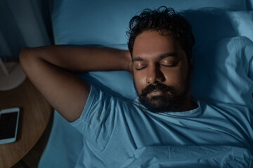 people, bedtime and rest concept - indian man sleeping in bed at home at night