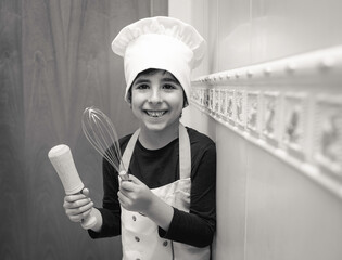 Naklejka premium Smiling boy poses in the kitchen of his house with chef uniform Conceptual of lifestyle