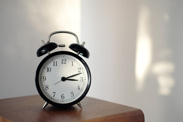 black alarm clock on wooden shelf with afternoon sun in the background