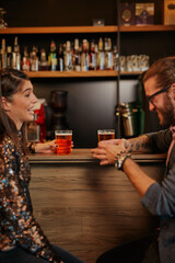 Group of cheerful friends standing near bar counter, drinking beer and chatting.