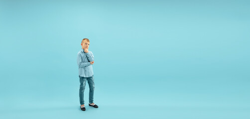 Thoughtful. Childhood and dream about big and famous future. Pretty little boy isolated on blue studio background. Childhood, dreams, imagination, education, facial expression, emotions concept. Flyer