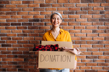 A smiling senior asian female volunteer holds a cardboard box with a donation, for reuse or recycle...