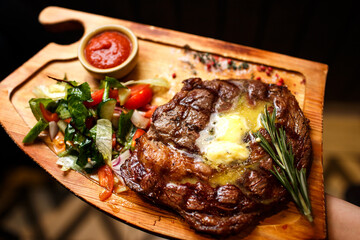 juicy fried steak with butter and pickled vegetables on a wooden board on a dark background