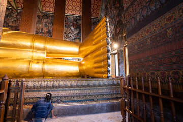 woman cleaning a big buddha gold statue at Wat Pho, Bangkok, Thailand.
