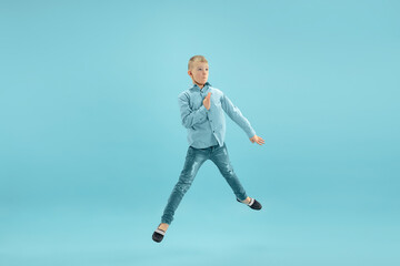 Fototapeta na wymiar Jumping high. Childhood and dream about big and famous future. Pretty little boy isolated on blue studio background. Childhood, dreams, imagination, education, facial expression, emotions concept.