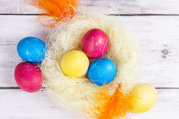 Fototapeta na wymiar Top view of colorful painted Easter eggs decorations in the nest on light wooden background.
