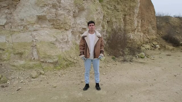 A young guy in a jacket and jeans pose an abandoned stone carier