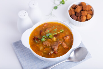 Pea soup with meat, smoked sausage, pea sprouts and croutons. Traditional Russian dish. Home kitchen. Close-up, selective focus.