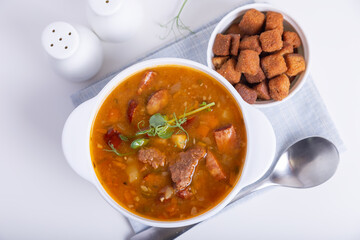 Pea soup with meat, smoked sausage, pea sprouts and croutons. Traditional Russian dish. Home kitchen. Close-up, selective focus.
