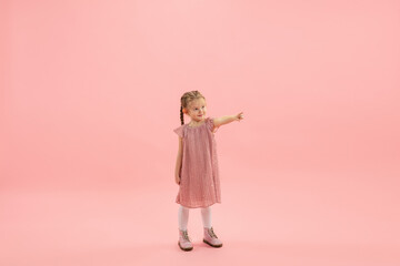 Pointing. Childhood and dream about big and famous future. Pretty longhair girl on coral pink studio background. Childhood, dreams, imagination, education, facial expression, emotions concept.